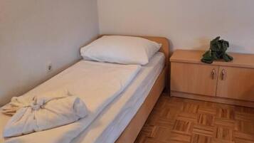 A single bed with a wooden headboard, a small wooden nightstand with a green object on it, and a herringbone-patterned wooden floor.