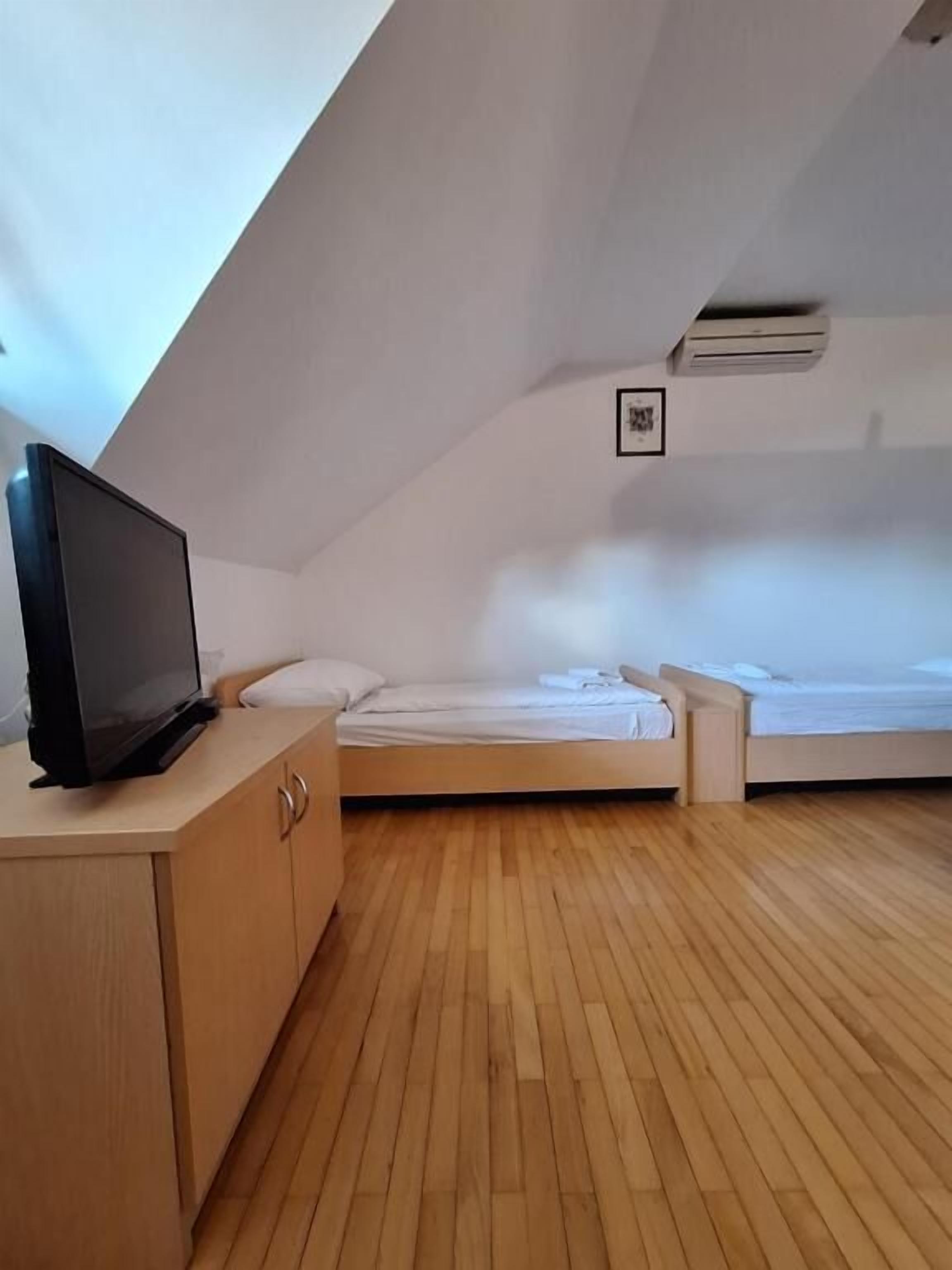 Um quarto com teto inclinado, uma TV sobre um armário de madeira, duas camas e um aparelho de ar condicionado.