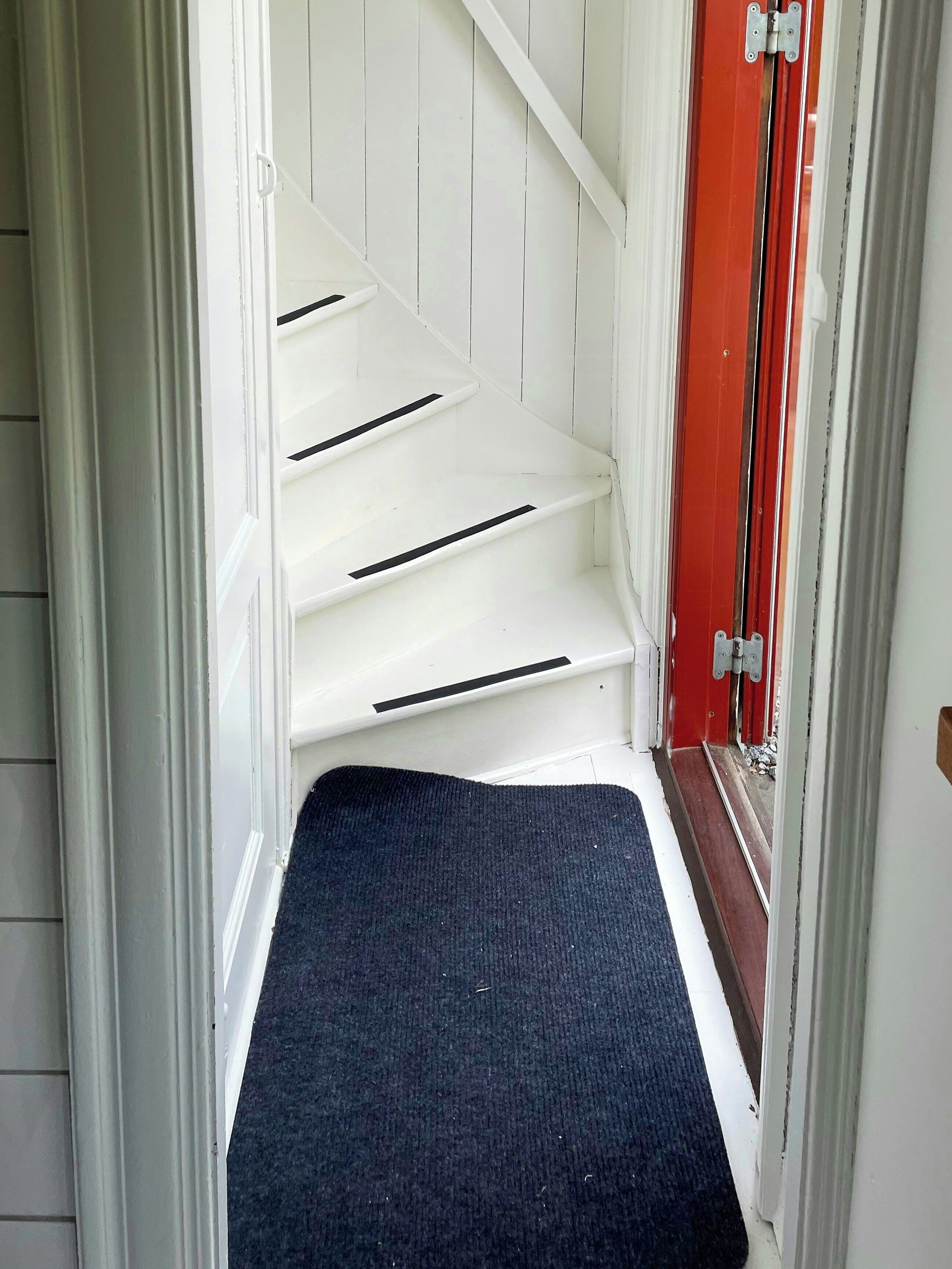Una escalera estrecha con paredes blancas y una puerta roja al final.