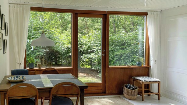 Comedor con mesa, sillas, lámpara colgante y vista a follaje a través de un ventanal corredero.