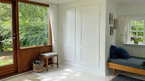 Una habitación con un banco de madera, una cesta de mimbre, un taburete pequeño, una ventana con cortinas y una puerta.
