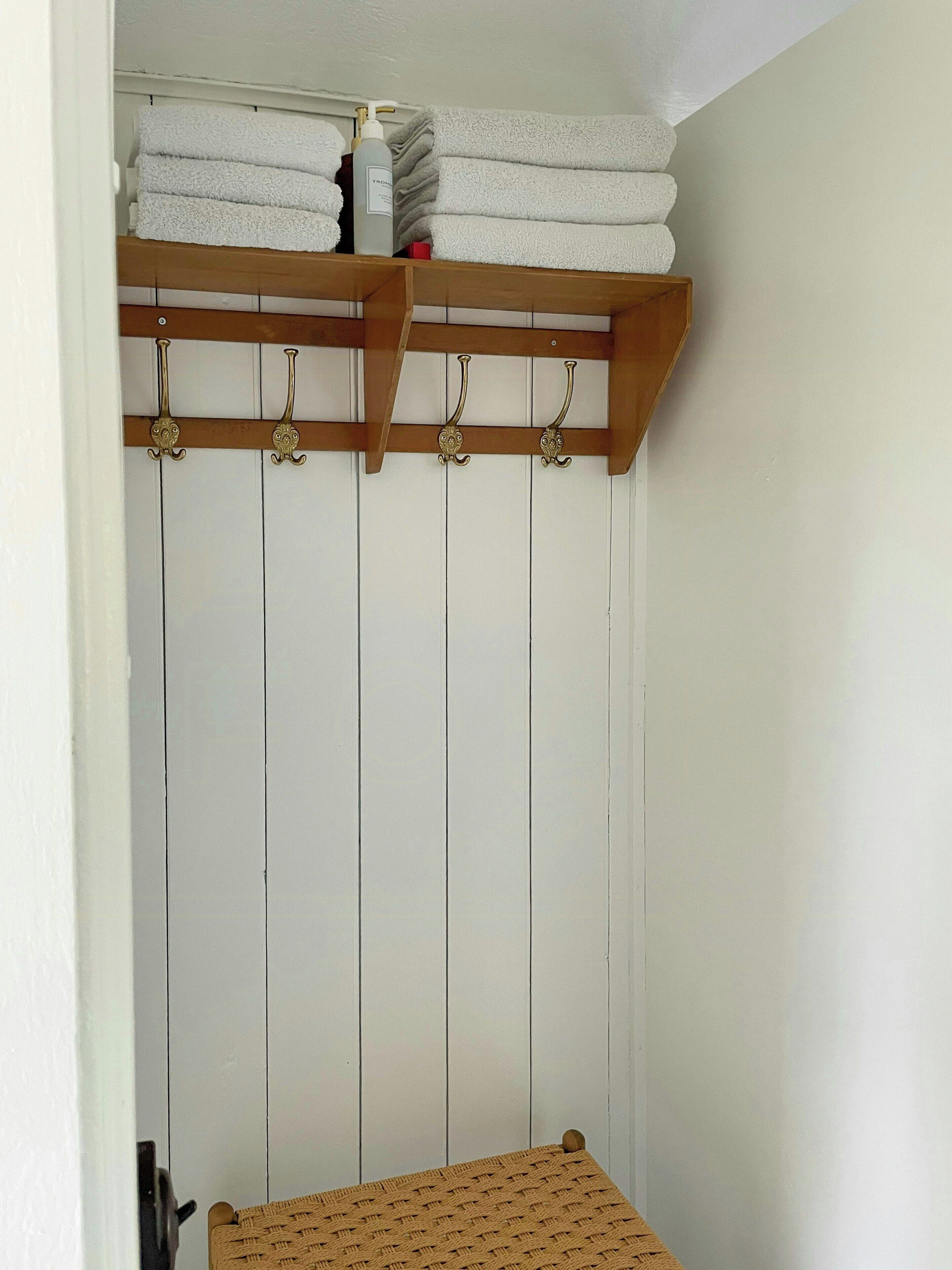 A room with a wooden shelf holding folded towels and a bottle of shampoo.
