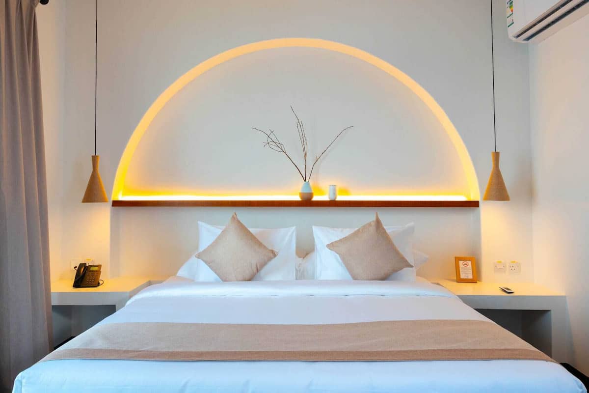 A hotel room with a bed, bedside tables, a phone, and a wall-mounted air conditioner.