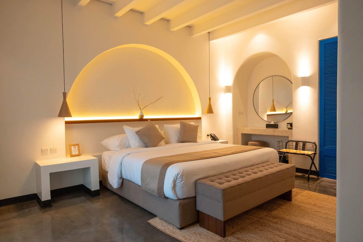 A modern bedroom with a large bed, bedside tables, a bench, and a mirror.