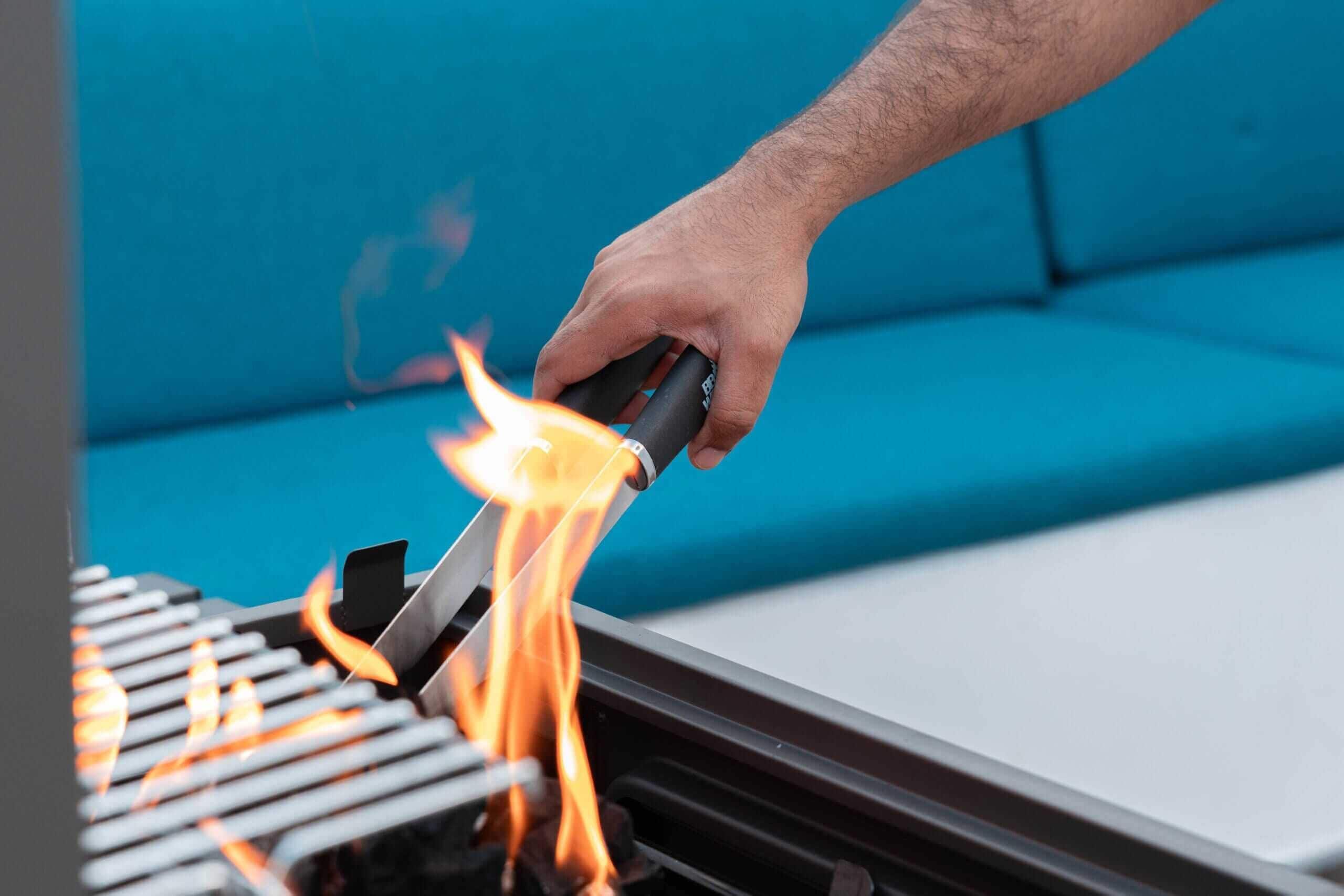 A hand holding a lighter over a grill with flames.