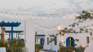 A building with blue arches and a pergola, string lights overhead, and a sign with Arabic text.