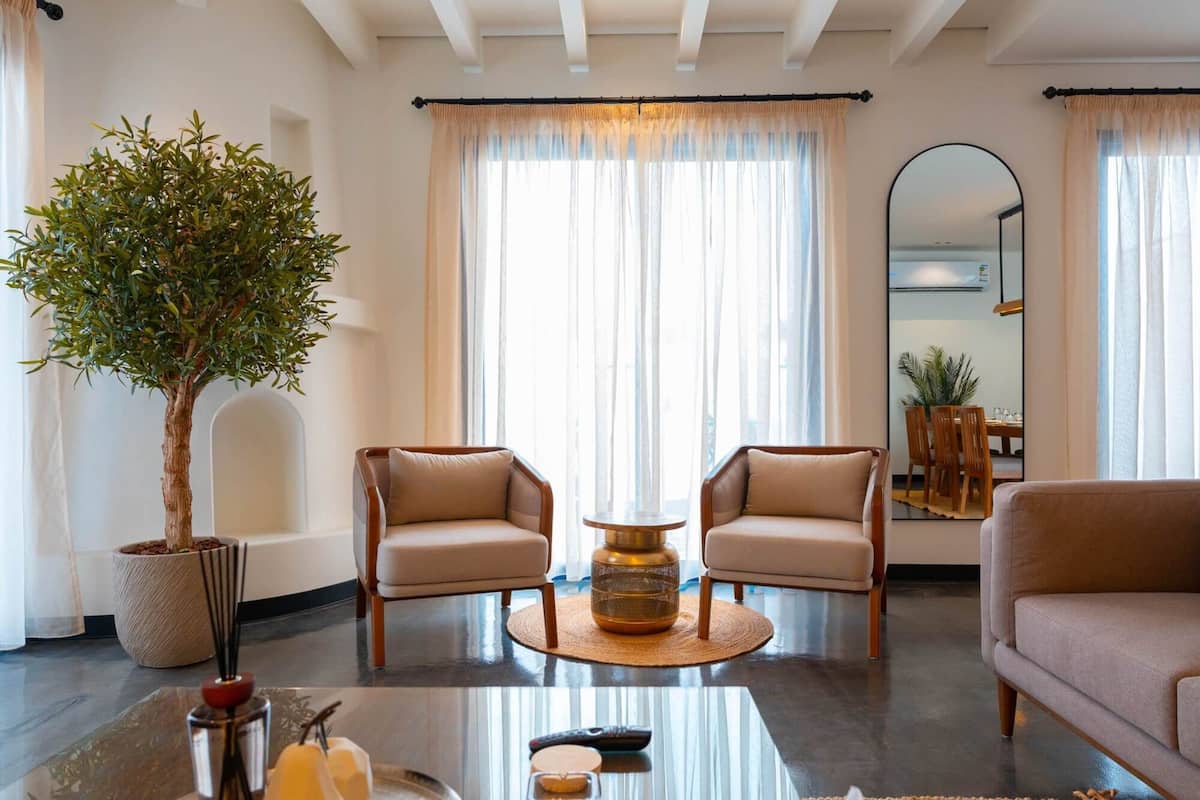 A living room with two armchairs, a round coffee table, a potted plant, and a large mirror.