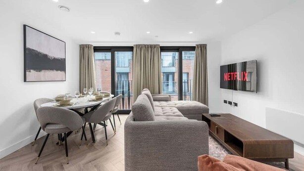 Una sala de estar moderna con comedor, un sofá, un televisor y ventanas amplias.
