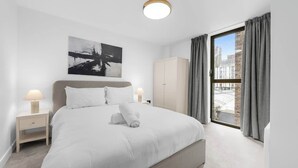 Una habitación de hotel moderna con una cama grande, una mesita de noche, un armario y vistas a la ciudad a través de la ventana.