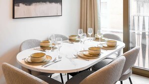 Un comedor con una mesa redonda preparada para cuatro personas, sillas, un cuadro en la pared y una ventana con cortinas.