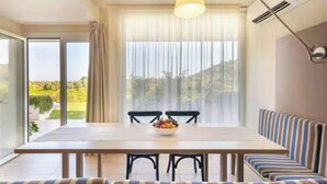 Ein Essbereich mit Tisch, Stühlen, einer Obstschüssel, einer Couch und einem großen Fenster mit Vorhängen.