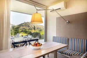 Ein Essbereich mit Tisch, Stühlen, einer Obstschale, einer Couch und Blick auf einen Hügel.