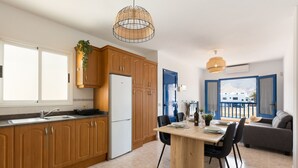 A modern kitchen with wooden cabinets, a dining area with a table and chairs, and a view of the outside through a door. - Famara Cactus by Escape Home (Famara)