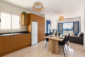 Une cuisine moderne avec des meubles en bois, un coin repas comprenant une table et des chaises, et une vue sur l’extérieur par une porte.