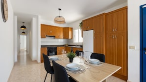 A modern kitchen with wooden cabinets, a dining table set for four, and a hanging light fixture. - Famara Cactus by Escape Home (Famara)