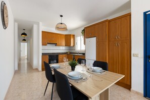 Une cuisine moderne avec des meubles en bois, une table à manger pour quatre personnes et un luminaire suspendu.