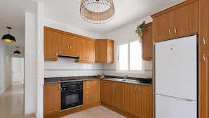 A modern kitchen with wooden cabinets, a built-in oven, a white refrigerator, and a hanging light fixture. - Famara Cactus by Escape Home (Famara)
