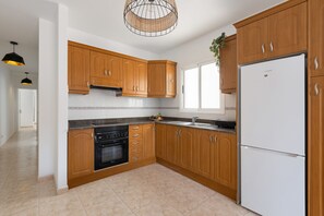 Une cuisine moderne avec des meubles en bois, un four encastré, un réfrigérateur blanc et un luminaire suspendu.