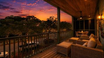 A wooden deck with wicker furniture, a view of trees, and a sunset.