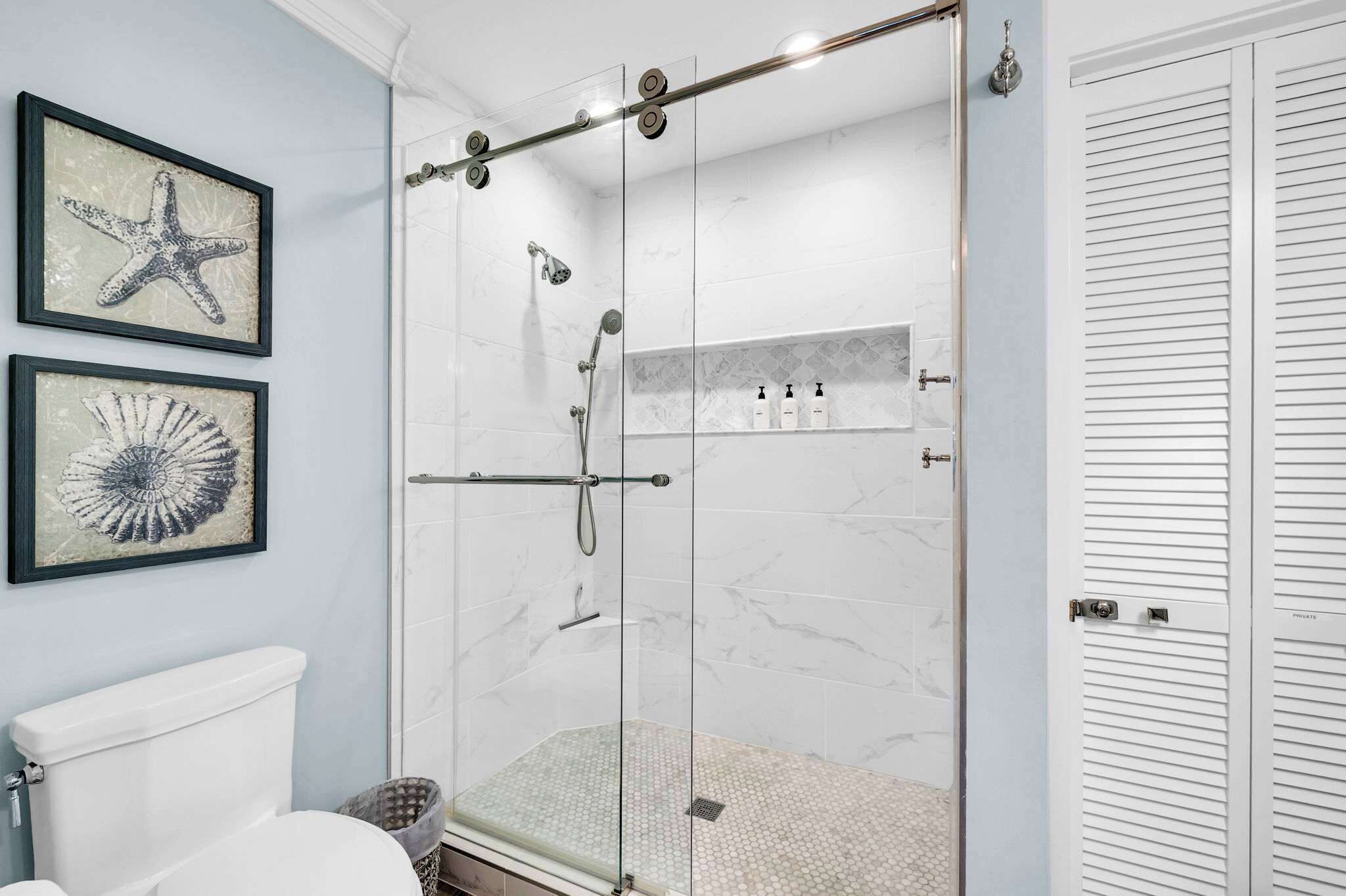 Une salle de bain dotée d’une douche à parois de verre, de toilettes et d’œuvres d’art encadrées accrochées au mur.