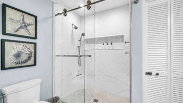 Une salle de bain dotée d’une douche à parois de verre, de toilettes et d’œuvres d’art encadrées accrochées au mur.