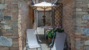 Een terras buiten met twee loungestoelen, een tafel met zonnescherm en een bakstenen muur.