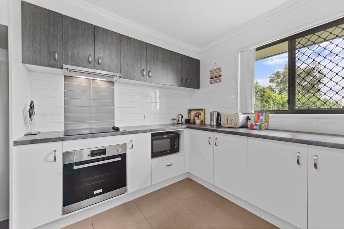 A modern kitchen with white cabinets, a microwave, an oven, and a window with a view of trees.