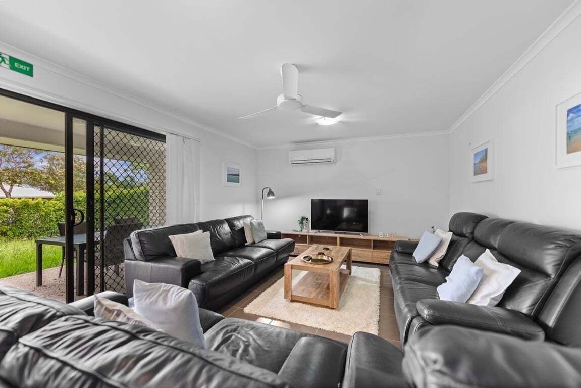 A modern living room with leather sofas, a coffee table, a flat-screen TV, and a ceiling fan.