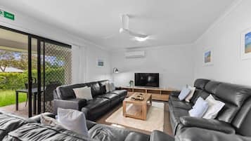 A modern living room with leather sofas, a coffee table, a flat-screen TV, and a ceiling fan.