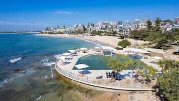 A coastal resort with a swimming pool, beach, and residential buildings in the background.