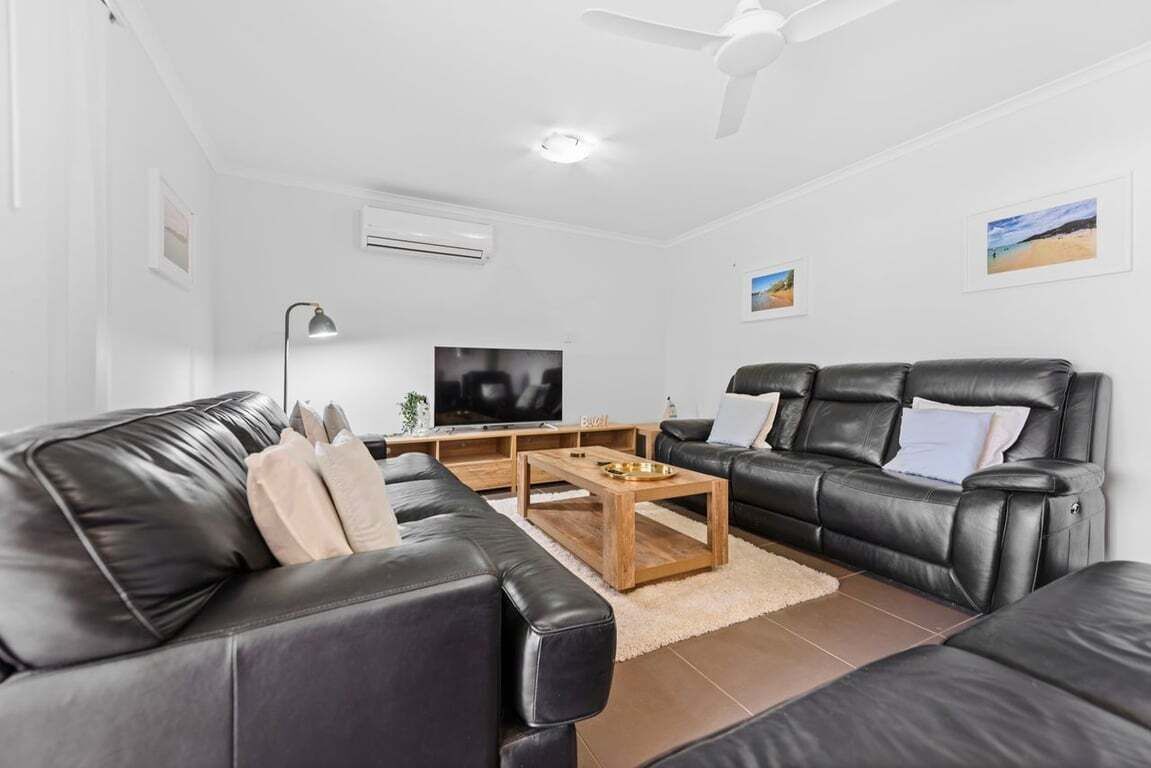 A modern living room with leather sofas, a wooden coffee table, a flat-screen TV, and a ceiling fan.