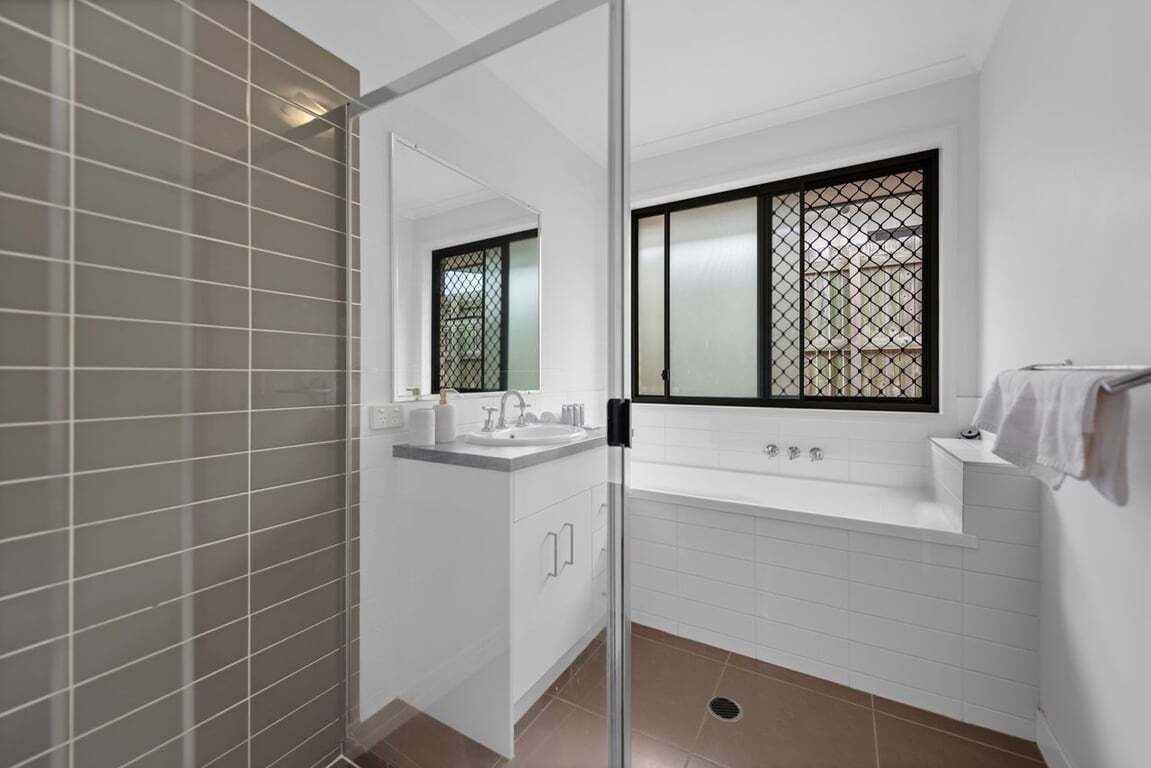 A modern bathroom with a glass shower enclosure, a white sink with a mirror, and a bathtub with a window.