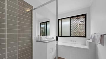 A modern bathroom with a glass shower enclosure, a white sink with a mirror, and a bathtub with a window.