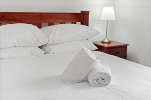 A neatly made bed with white linens, a wooden headboard, and a bedside table with a lamp. - Sunny Coast 3BR Family Hinterland Retreat (Little Mountain)