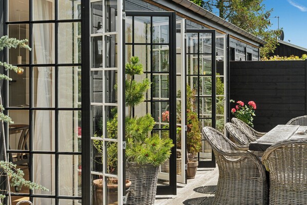 A modern house with large glass windows, wicker furniture, and potted plants.