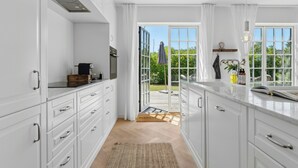 Una cocina moderna con armarios blancos, encimera de madera y vistas a un espacio exterior a través de puertas de cristal.