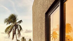 A building with a textured facade and a large window reflecting palm trees and a sunset. - Gamboa Oasis Patacho 180m from the beach on the Ecological Route of Miracles (Porto de Pedras)