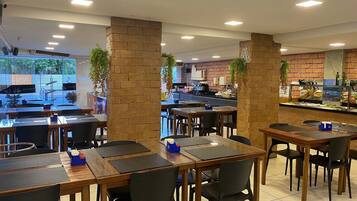 Un ristorante con pilastri in mattoni, tavoli con sedie nere e un banco buffet.