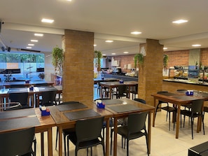 Ein Restaurant mit Backsteensäulen, Tischen mit schwarzen Stühlen und einer Buffettheke.