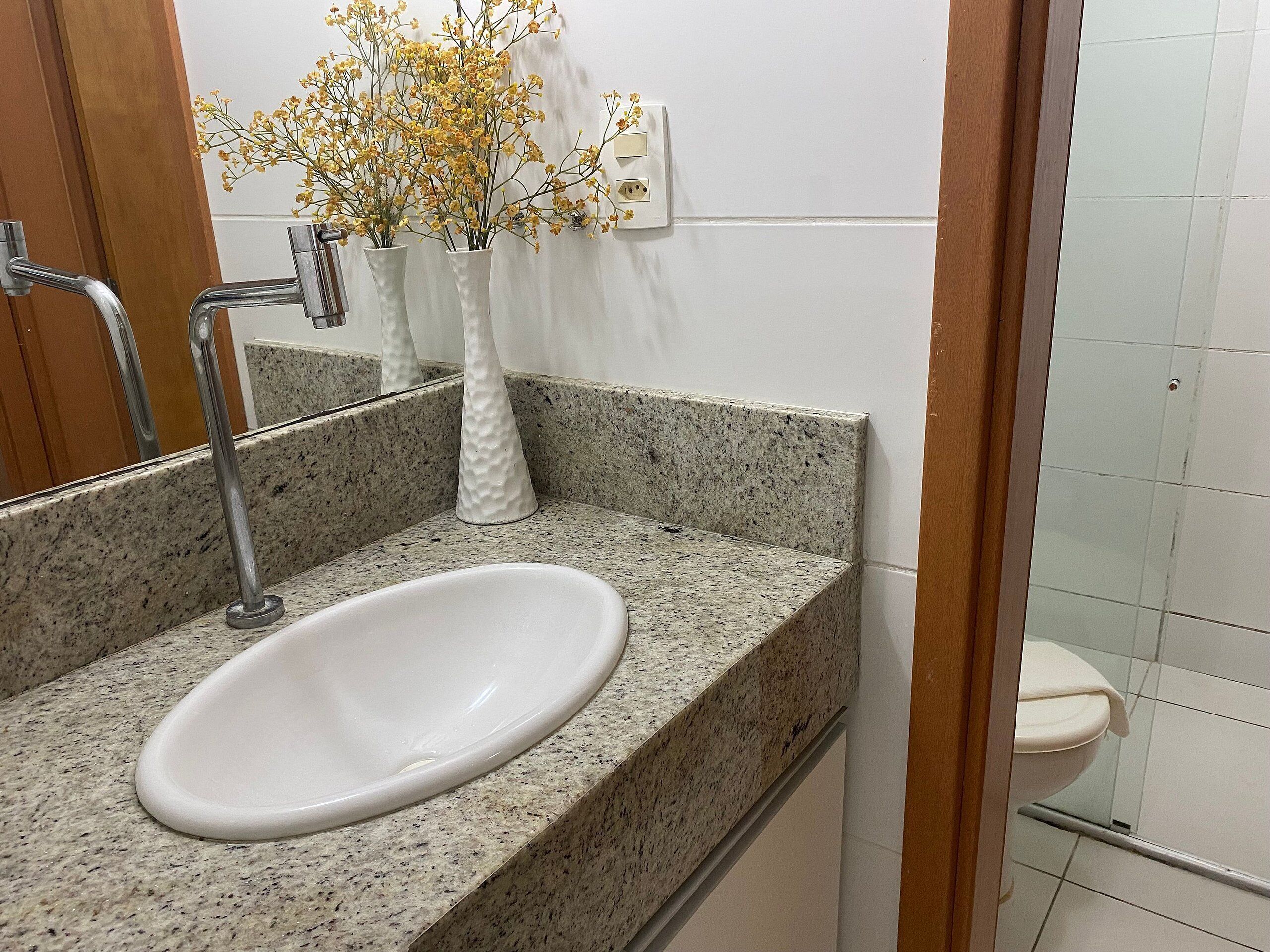 Un baño con encimera de granito, un lavamanos blanco, un espejo y un florero con flores amarillas.