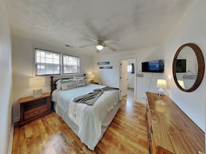 Ein Schlafzimmer mit Bett, Nachttischen, Deckenventilator, Fernseher, Spiegel und einer Tür.