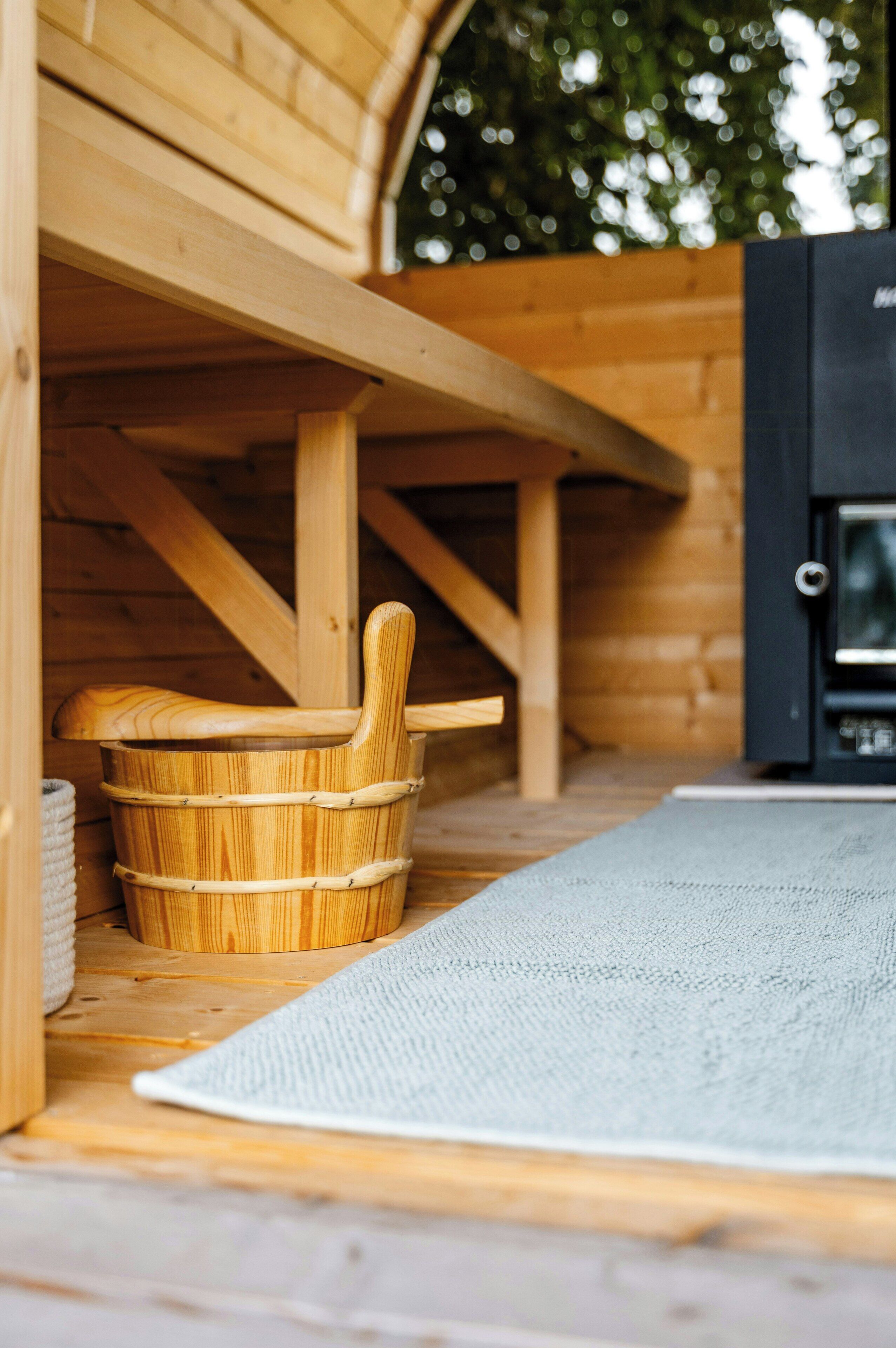 Een houten sauna met een houten bank en een grote emmer.