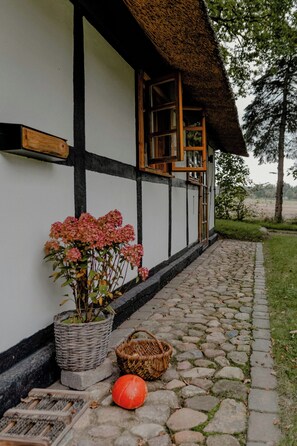 A traditional building with a thatched roof, a stone pathway, and a potted plant with pink flowers. - Romantic nights under the thatched roof (Scharnebeck)