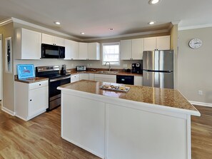 A modern kitchen with white cabinetry, granite countertops, stainless steel appliances, and a central island. - Starboard Shores | In-Town Coastal Retreat (Surf City)