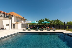A swimming pool with lounge chairs and umbrellas, a white building with a tiled roof, and a fenced yard with trees. - Villa Flora Zadar Villas (Benkovac)