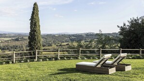 Un espace verdoyant, délimité par une clôture en bois, avec deux fauteuils de jardin en osier et une vue sur un paysage vallonné.