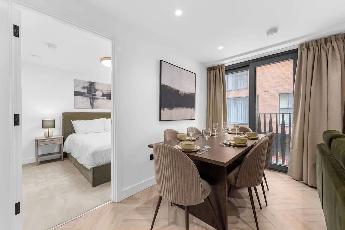 A hotel room with a dining area, a bed, a nightstand, a lamp, and a window with curtains.