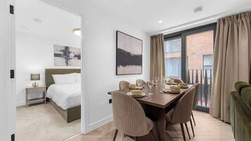 A hotel room with a dining area, a bed, a nightstand, a lamp, and a window with curtains.