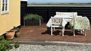Een terras met een tafel en stoelen, planten in potten, en uitzicht op het landschap.