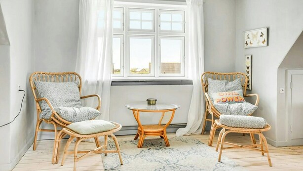 Een kamer met twee rieten stoelen, een klein rond tafeltje en een raam met witte gordijnen.